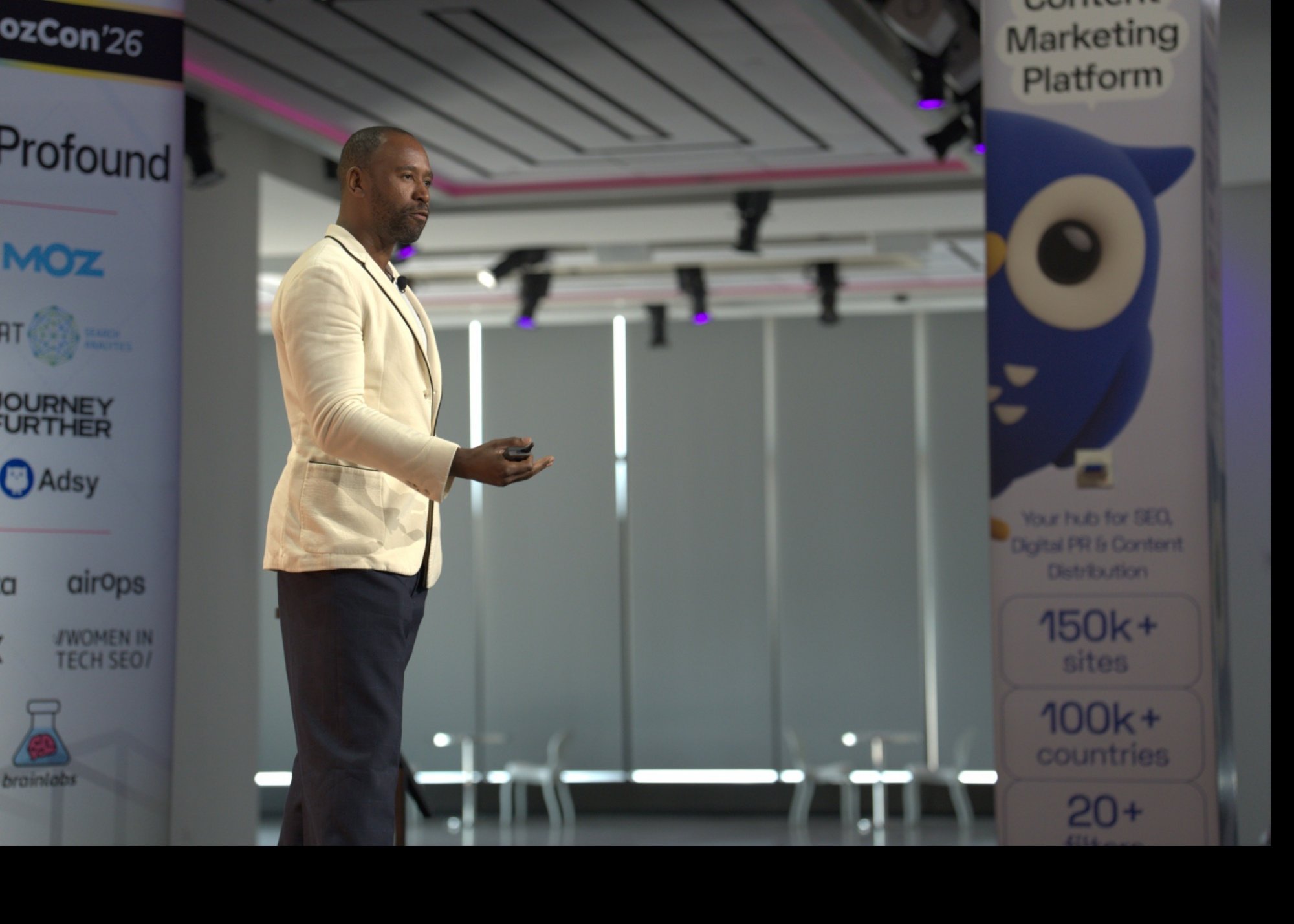 Mike King presenting on stage at MozCon 2026 with Adsy branded column in the background