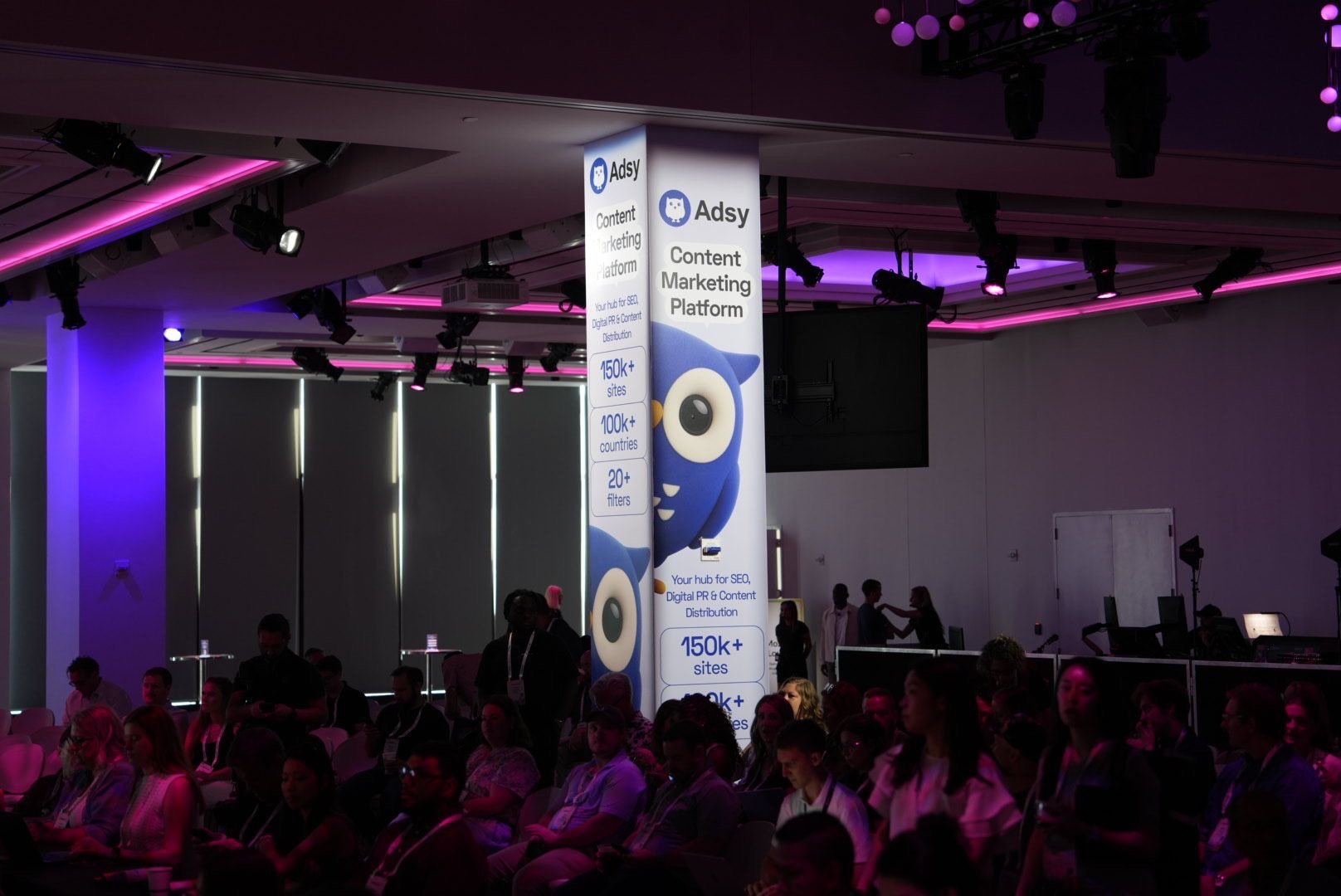 Adsy branding at MozCon 2026 conference hall with audience and illuminated content marketing platform banner